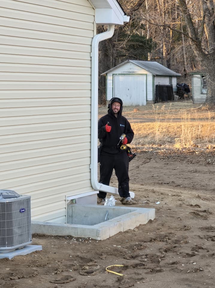 Crew member installing a downspout against a bright morning home
